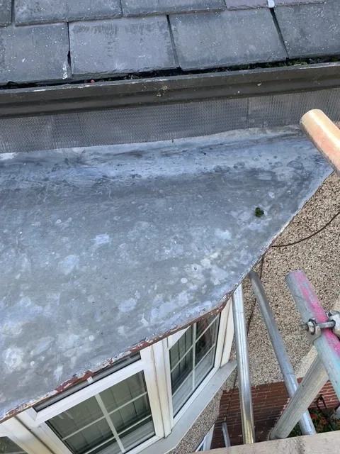 Before: the worn grey covering on the roof of a bay window, seen from the scaffold beneath a slate roof