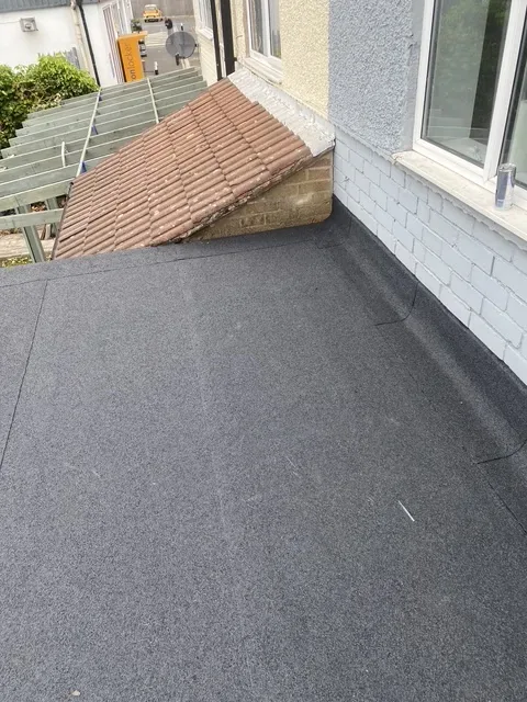 After: the same flat roof re-covered by Wales Roofing in new mineral felt, dressed up the wall beneath a window