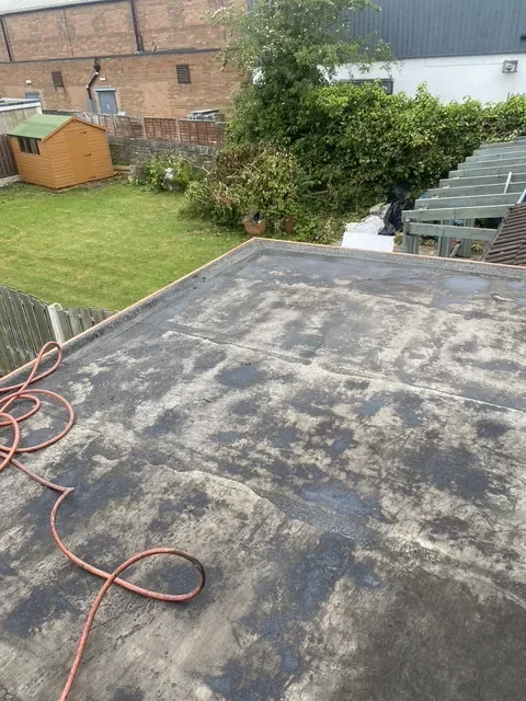 Before: an old flat roof with worn, patchy felt where water has been standing, looking over a back garden